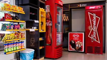 Zona de máquinas expendedoras con refrigeradores de Coca-Cola y Budweiser, y diversas opciones de bocadillos y bebidas.