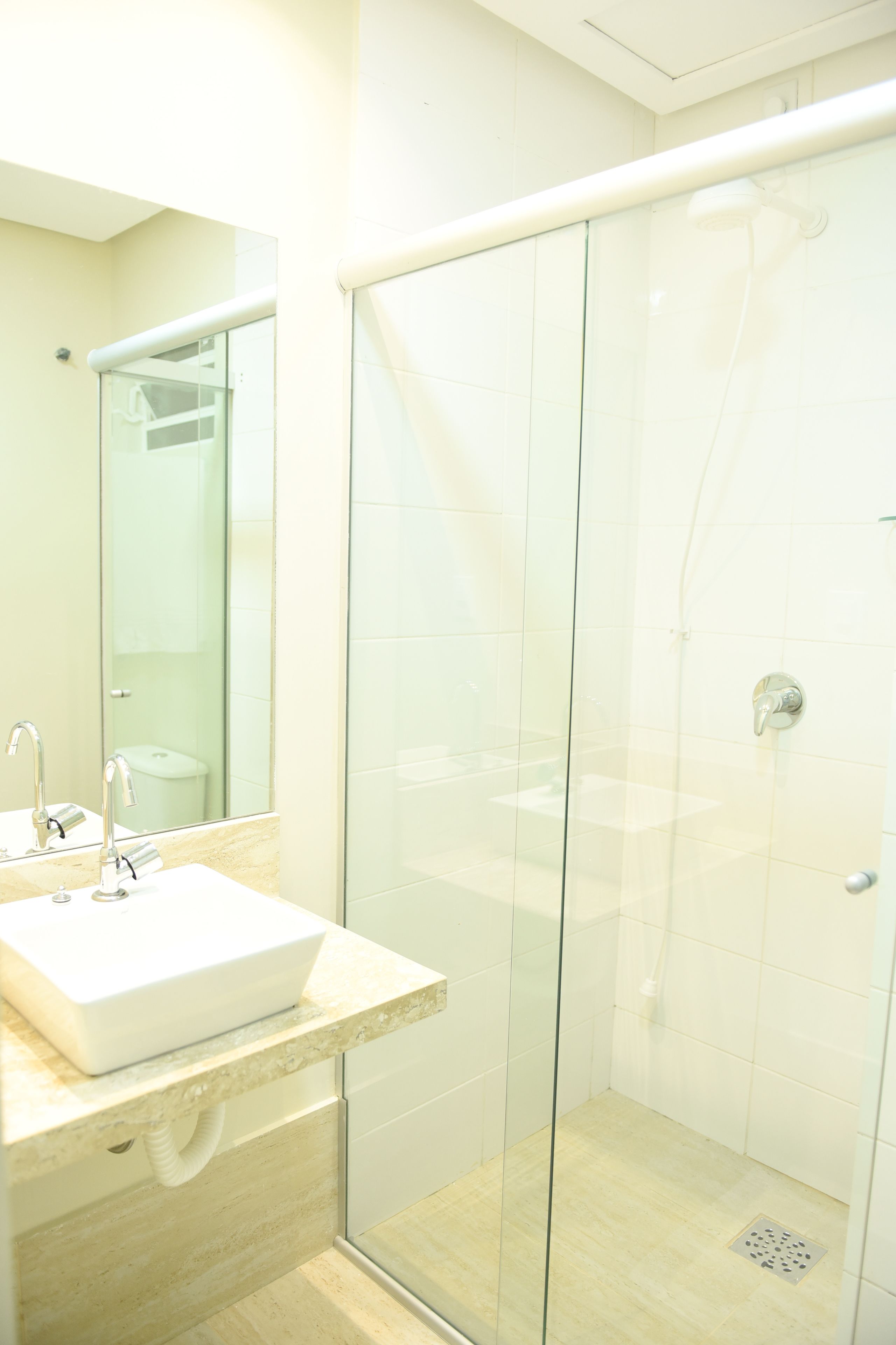 A modern bathroom with a glass-enclosed shower, a sink with a mirror, and a light-colored tiled floor.