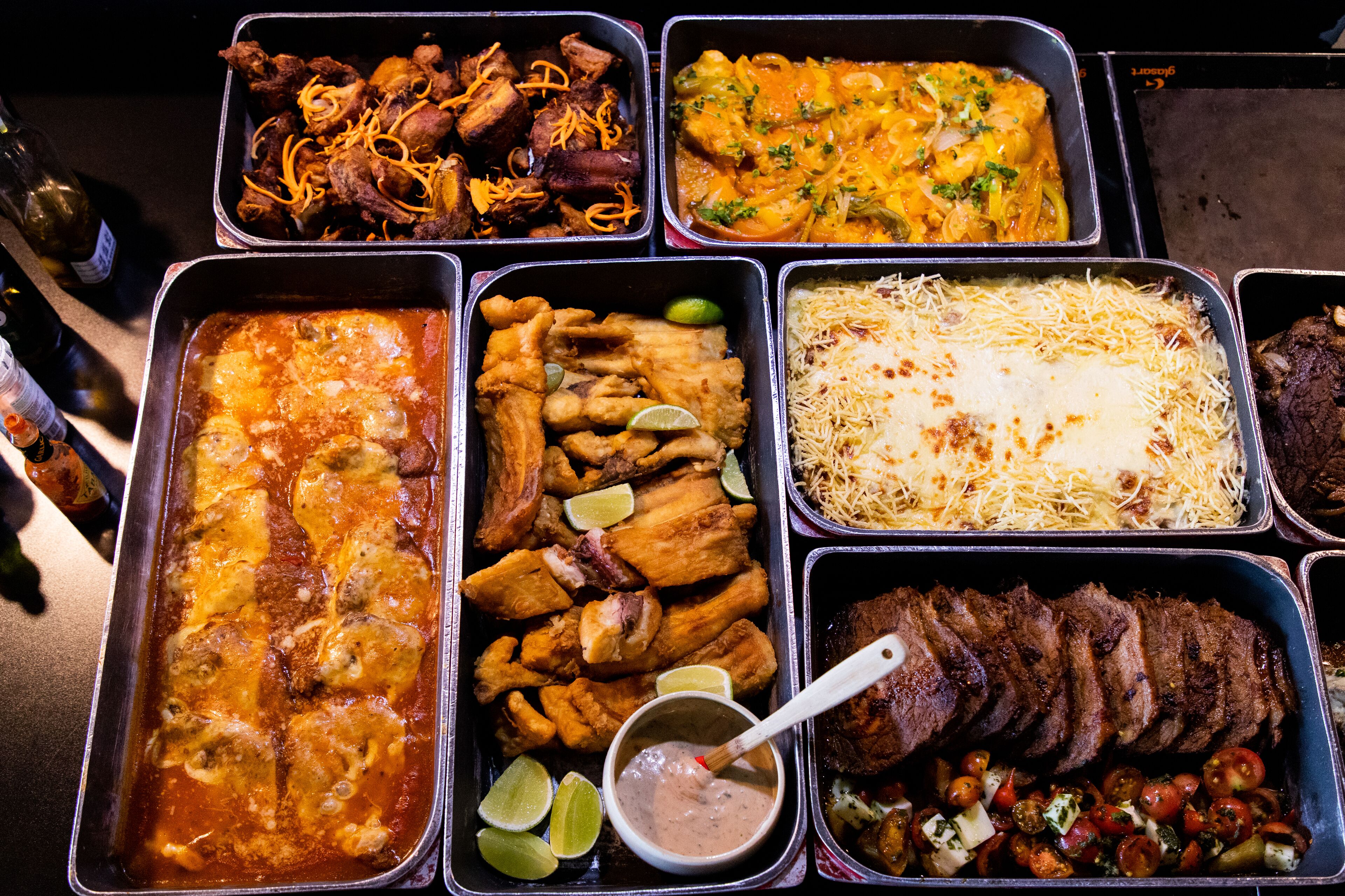A variety of food dishes in metal trays, including meat, fish, and vegetables.