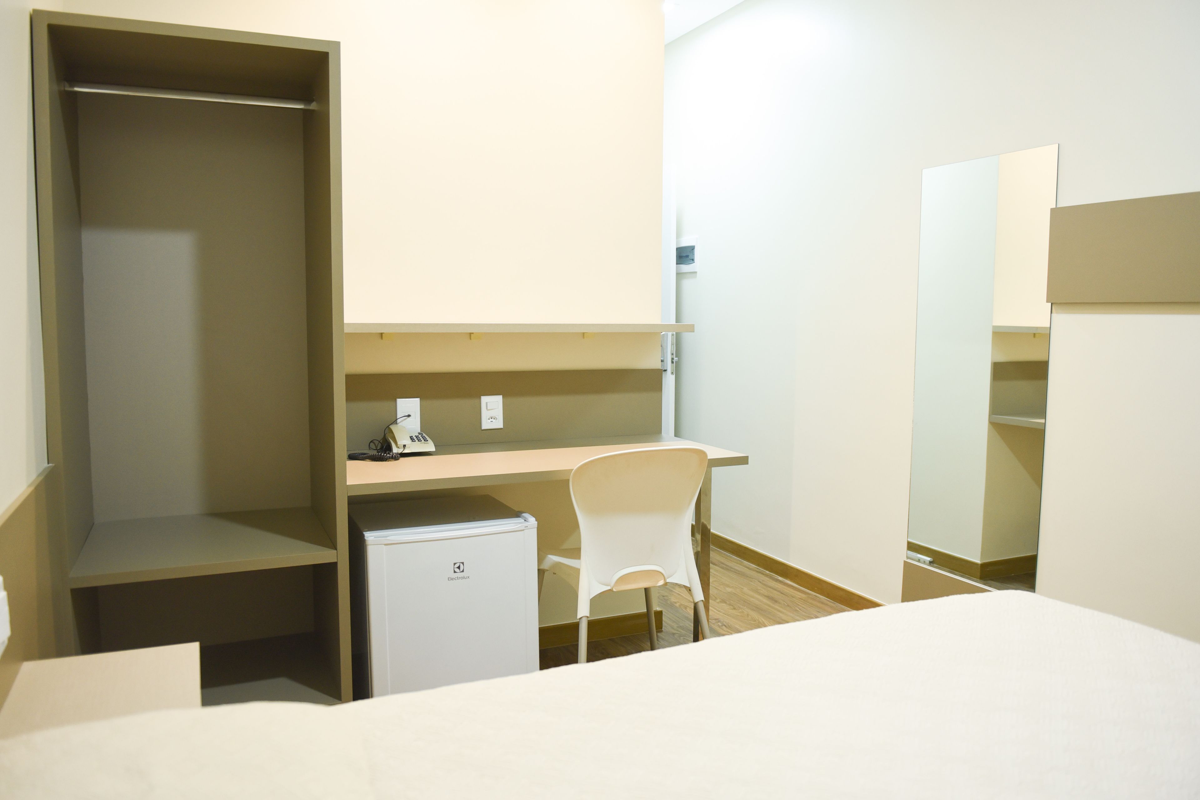 Una habitación de hotel con cama, escritorio, silla, armario y un refrigerador pequeño.