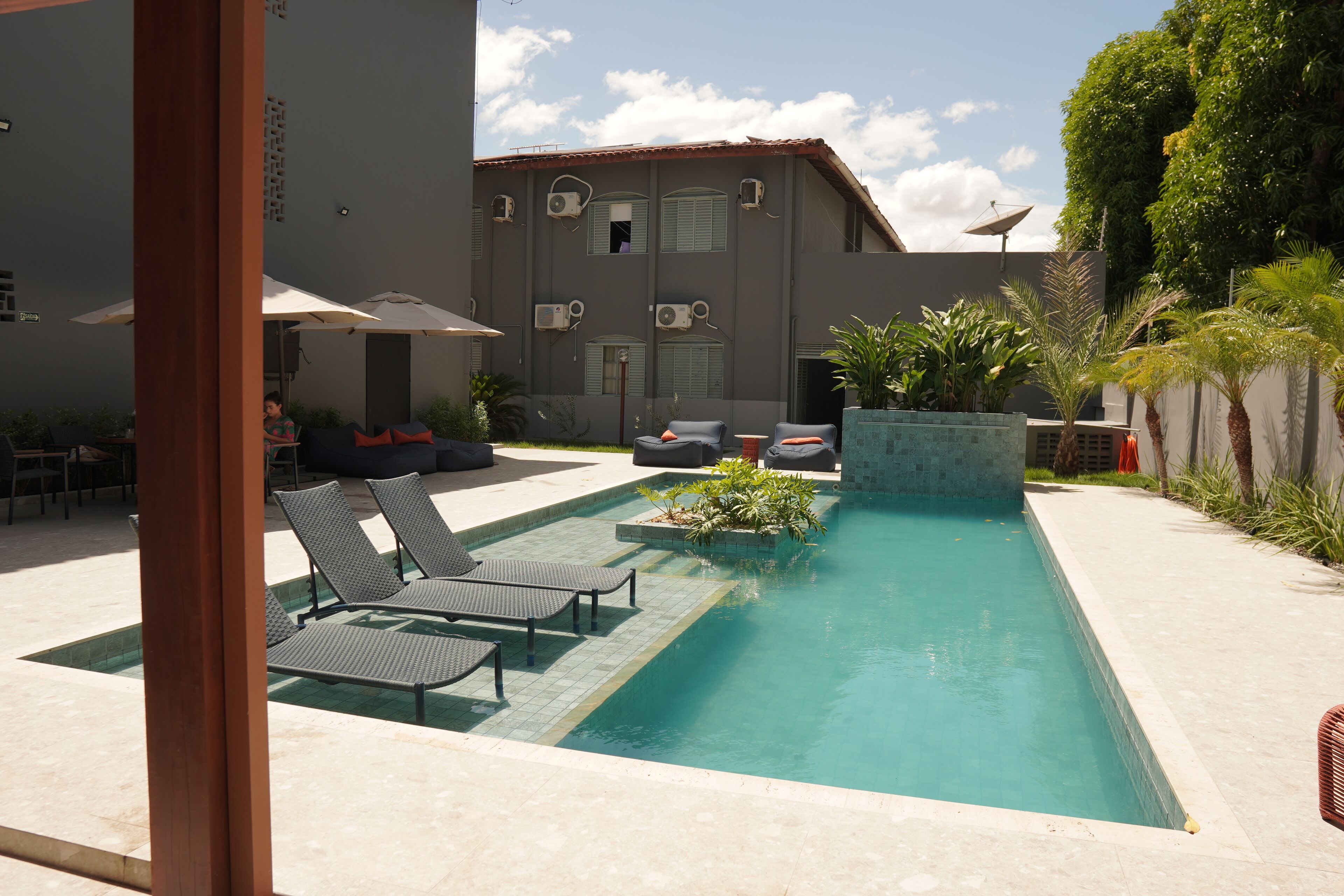 A swimming pool with lounge chairs, a small garden area, and a building with multiple air conditioning units.