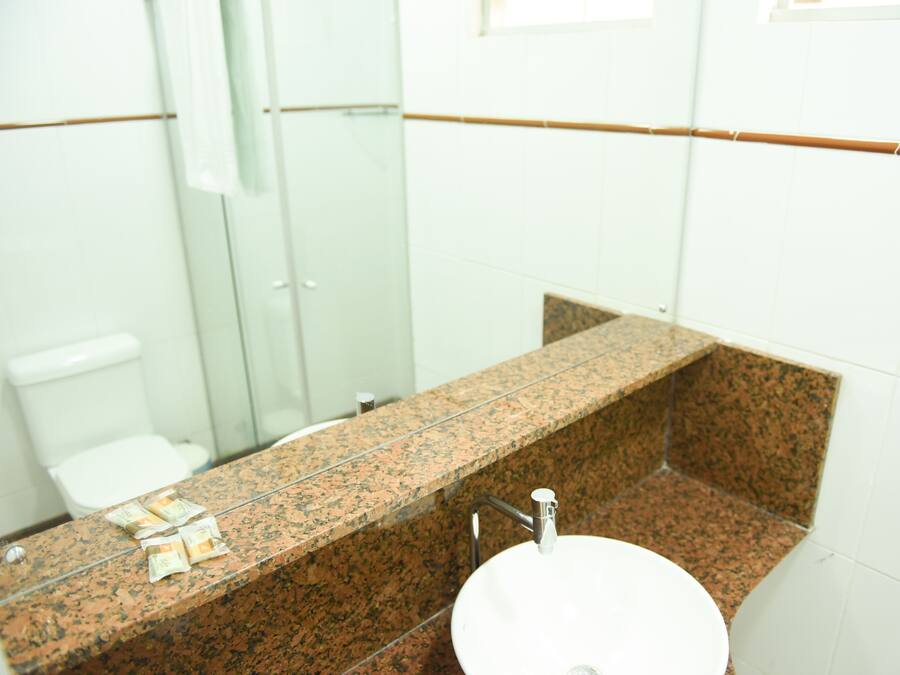 Un baño con encimera de granito, un lavamanos blanco y una mampara de vidrio para la ducha.