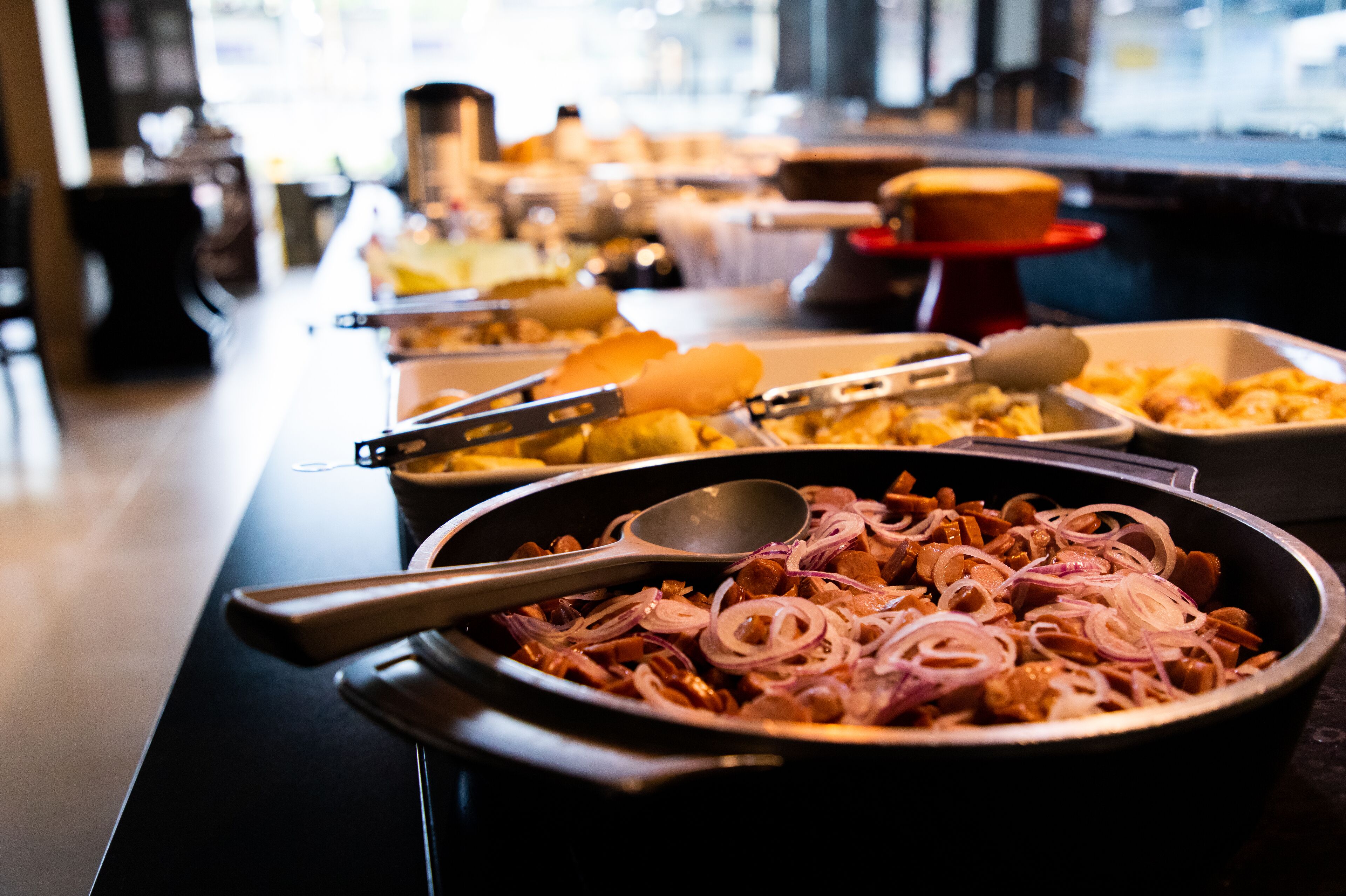 A buffet with various dishes, including a pan with sliced onions and meat.