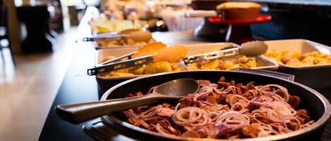 A buffet with various dishes, including a pan with sliced onions and meat.