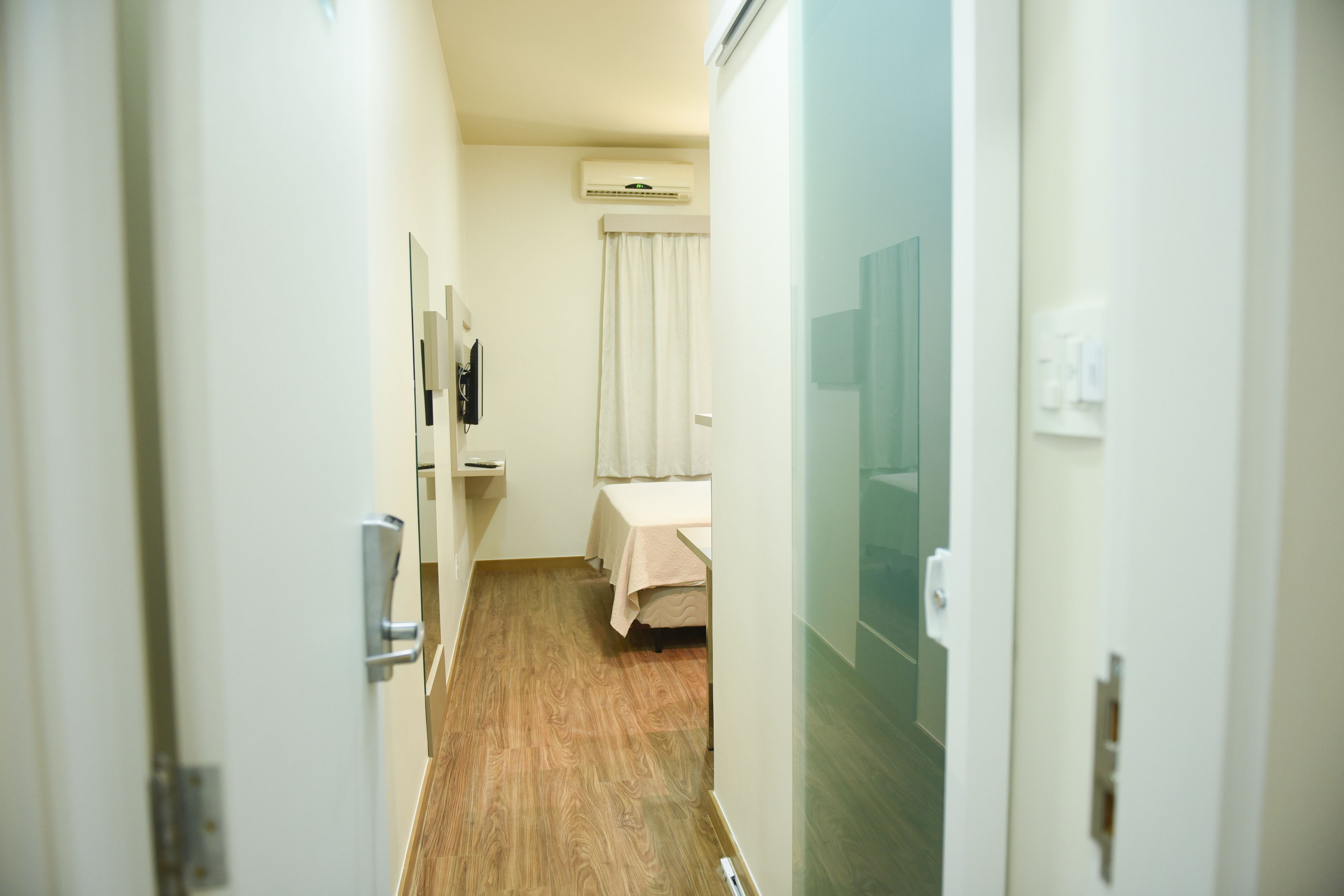 A narrow hallway leading to a room with a bed, a small table, and an air conditioning unit mounted on the wall.