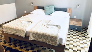 Una cama doble con ropa de cama estampada, cabecera de madera, mesita de noche con cajón y suelo a cuadros.