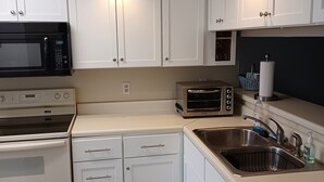 Una cocina con armarios blancos, un microondas, un tostador y un lavamanos.
