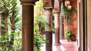 An indoor corridor with arches and columns, featuring potted plants and hanging lanterns.