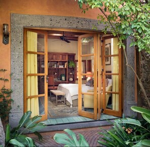 A room with a bed, a chair, and a desk, with a view of a garden.