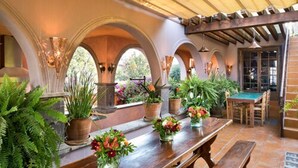 A covered patio with a wooden table, benches, and potted plants.