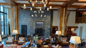 Eine geräumige Lobby mit Kamin aus Stein, Holzbalken und einer Kristallleuchter.
