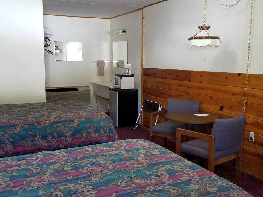 A hotel room with two beds, a small table with chairs, a wooden accent wall, and a hanging light fixture.