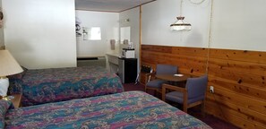 A hotel room with two beds, a small table with chairs, a wooden accent wall, and a hanging light fixture.