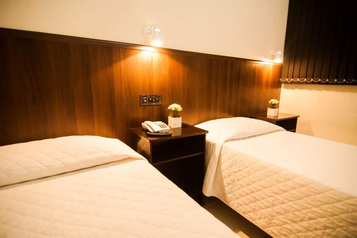 Une chambre d’hôtel avec deux lits, une tête de lit en bois, des tables de chevet avec des lampes et un téléphone sur l’une des tables.