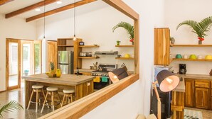 A modern kitchen with wooden beams, a central island with stools, a refrigerator, stove, and various kitchen appliances.