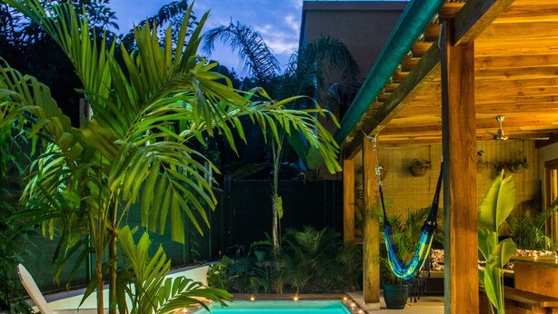 A wooden deck with a pool, surrounded by tropical plants and a hammock.