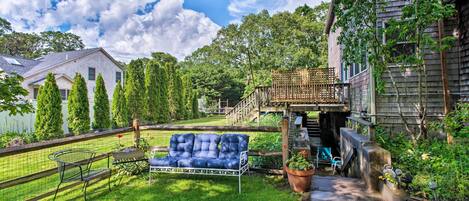 A backyard with a blue outdoor sofa, a wooden deck, and a brick pathway.