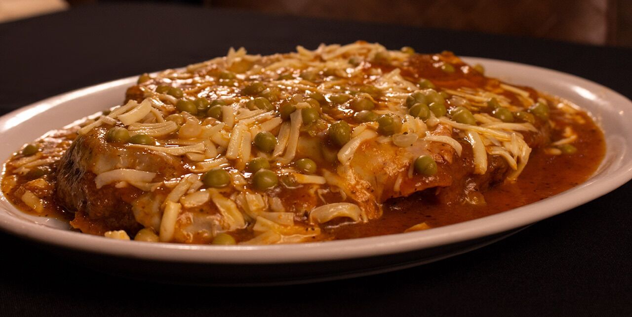 A plate of enchiladas with cheese and green peas on a white plate.