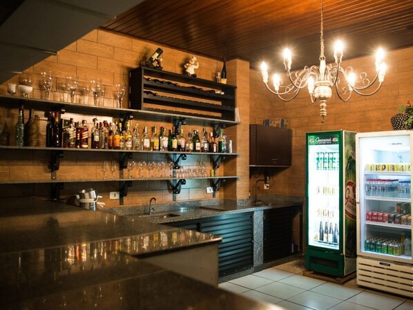 A bar area with shelves of bottles and glasses, a refrigerator, and a chandelier.