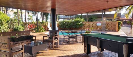 A pool area with a wooden deck, pool table, and seating.