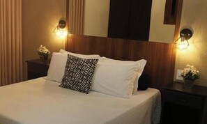 Una habitación de hotel con una cama, dos mesitas de noche y lámparas de pared.