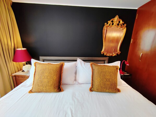A hotel room with a bed, two decorative pillows, a nightstand with a lamp, and a mirror on the wall.