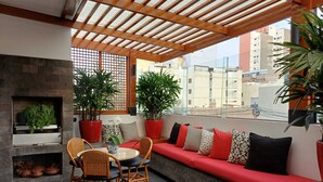 Un área de estar al aire libre acogedora, con una chimenea, plantas en macetas y vistas a la ciudad.