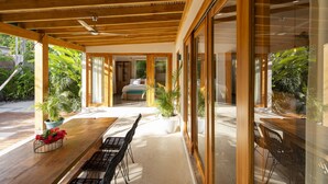A modern, open-plan living area with a wooden ceiling, large windows, and potted plants. - Tropical Boutique Sunset (Cóbano)