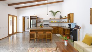 A spacious kitchen with wooden beams, a central island with stools, a refrigerator, and a coffee machine. - Tropical Boutique Sunset (Cóbano)