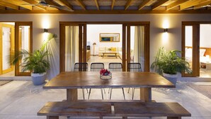 A dining area with a wooden table and benches, surrounded by chairs, with potted plants on either side. - Tropical Boutique Sunset (Cóbano)