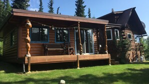 Eine Blockhütte mit Veranda, großen Fenstern und einem überdachten Sitzbereich im Freien.