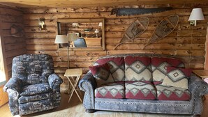 Ein gemütliches Blockhaus-Interieur mit einem gemusterten Sessel, einer gepolsterten Couch und einem kleinen Holztisch.