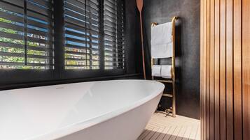 A modern bathroom with a freestanding bathtub, a wooden towel rack, and a view of greenery outside.