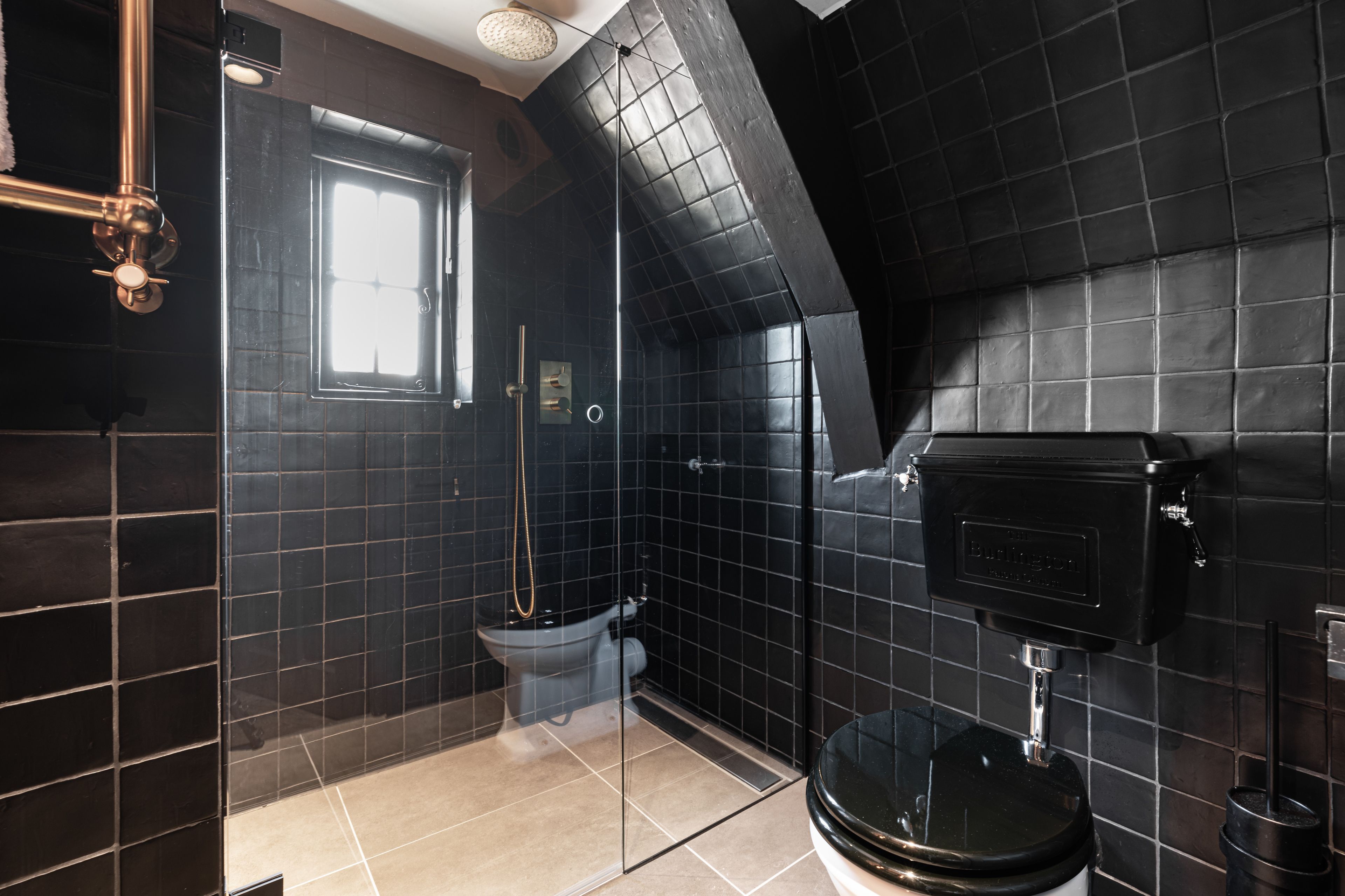 Une salle de bain moderne avec des carreaux noirs, une douche à l’italienne en verre, des toilettes et un lavabo.