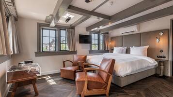 A modern bedroom with a large bed, wooden chairs, a glass table, and a TV on the wall.