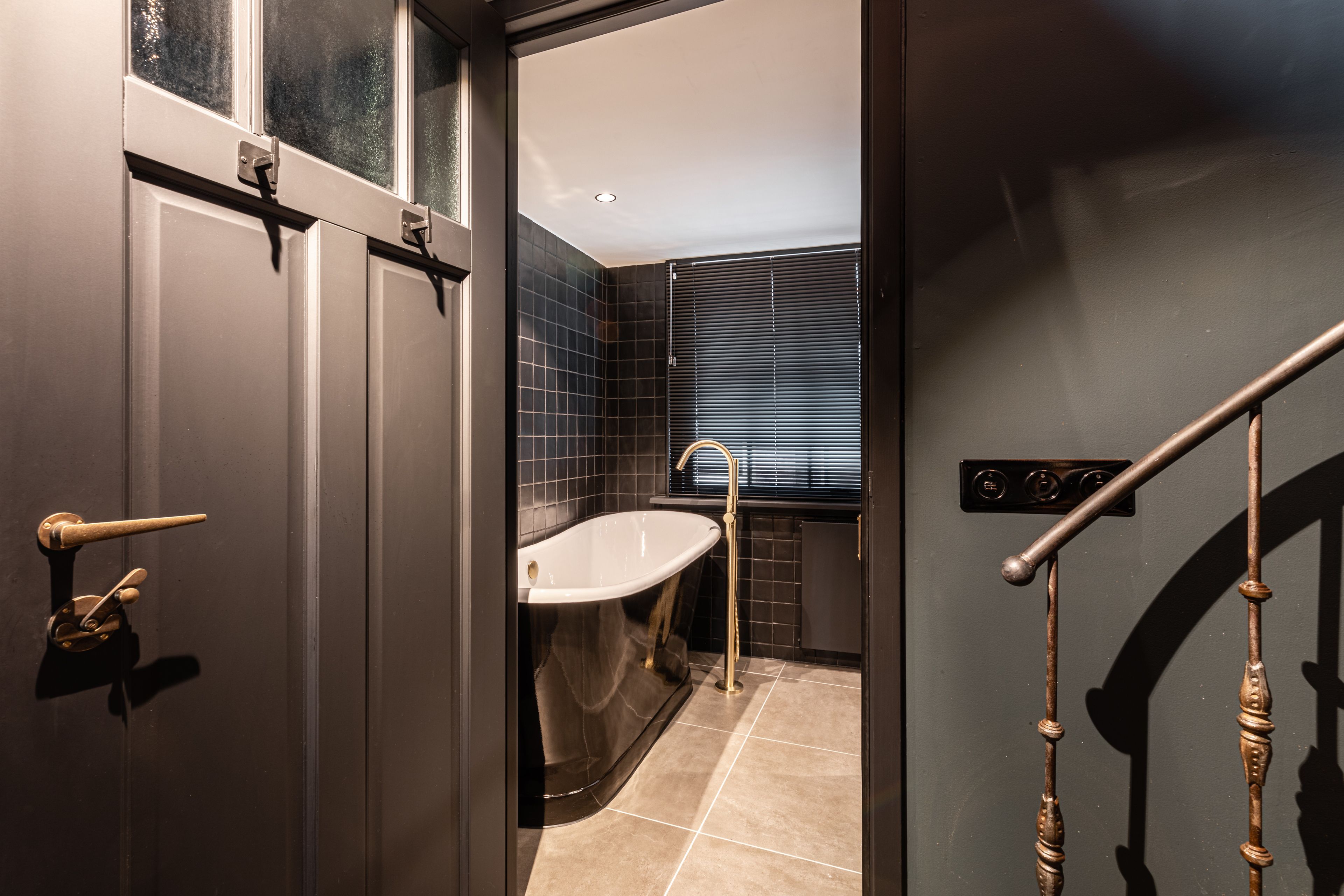 A modern bathroom with a bathtub, a sink, and a window with blinds.