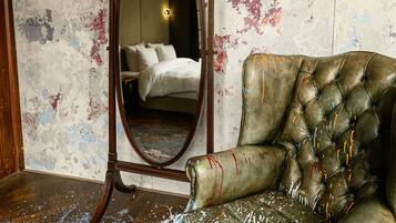 A room with a large mirror, a tufted leather armchair, and a bed with white linens.