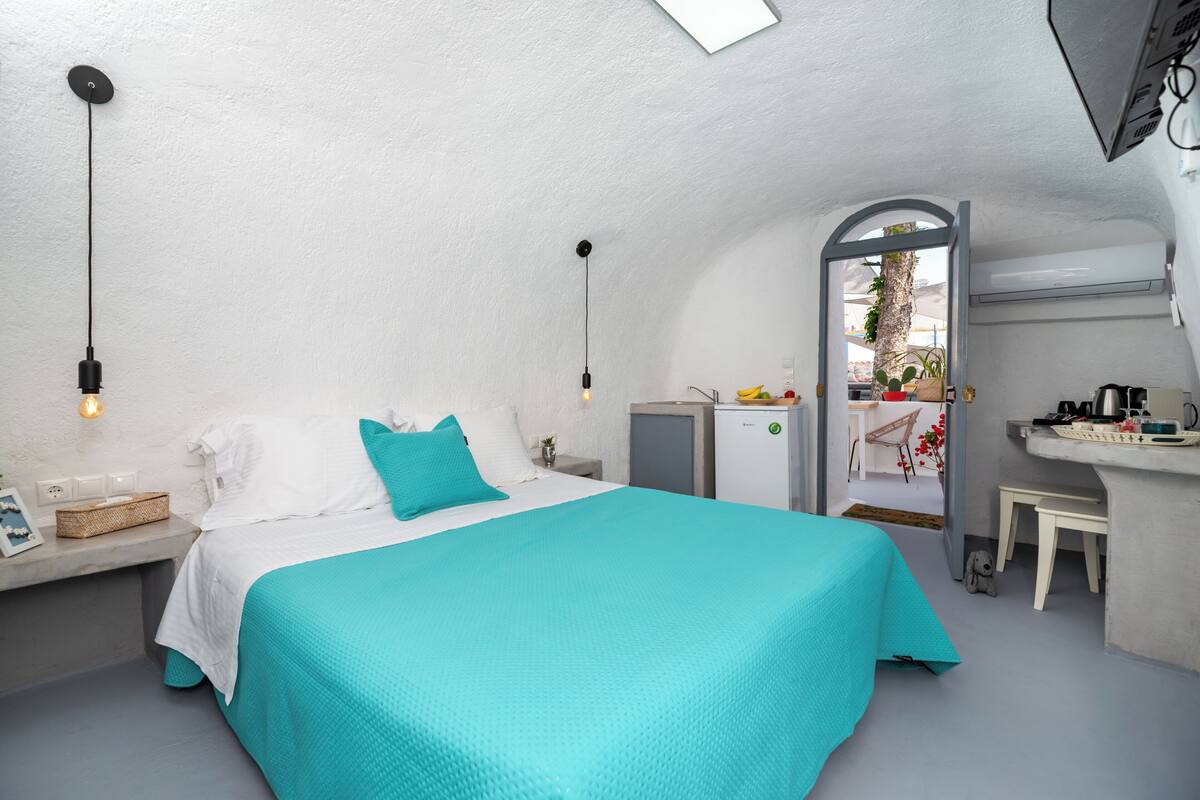 Ein Schlafzimmer mit Bett, Nachttisch, Lampe und Blick auf einen Balkon mit Pflanzen und einem Stuhl.