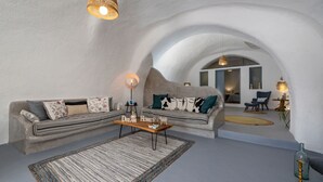 A cozy living room with a sofa, coffee table, and hanging light fixture. - 1812 Caves 'n Mansion (Santorini)