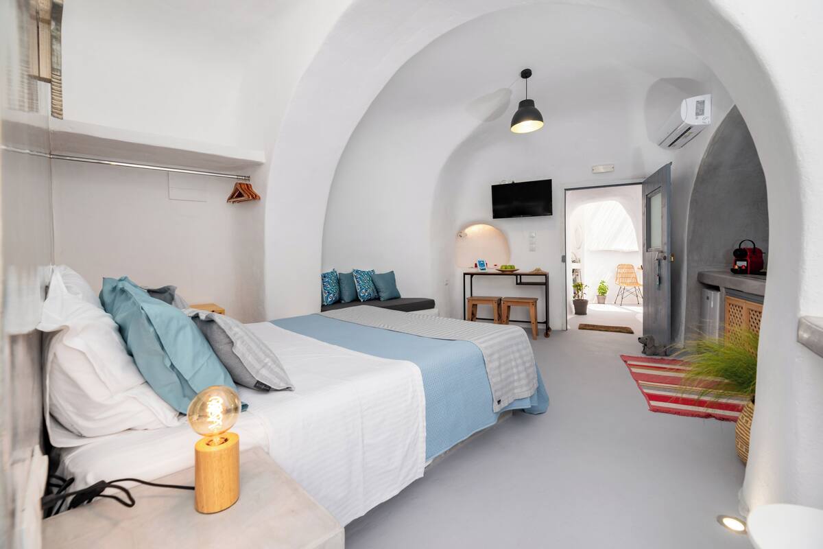 Ein modernes, minimalistisches Schlafzimmer mit zwei Betten, einem Flachbildfernseher und einer kleinen Küchenzeile.