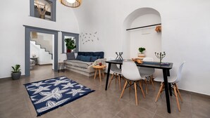 A modern living room with a dining area, featuring a staircase, a blue patterned rug, and a dining table with chairs. - 1812 Caves 'n Mansion (Santorini)