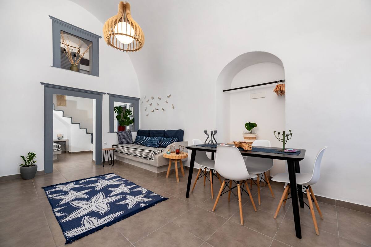 Ein modernes Wohnzimmer mit Essbereich, inklusive Treppe, einem blauen Teppich mit Muster und einem Esstisch mit Stühlen.