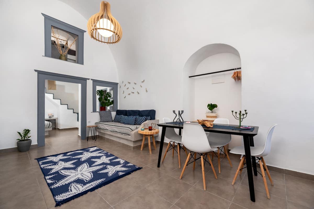 Uma sala de estar moderna com área de jantar, apresentando uma escada, um tapete azul estampado e uma mesa de jantar com cadeiras.