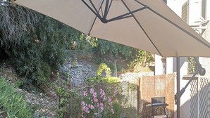 Un patio al aire libre con una mesa, sillas, una sombrilla grande y una parrilla.
