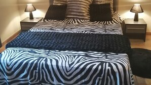 Una cama con ropa de cama estampada de cebra, dos lámparas de noche y un cuadro en la pared.
