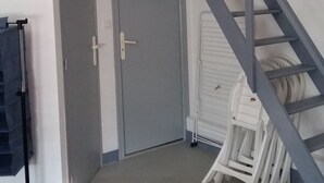 Une pièce avec une porte grise, un lit rouge, une chaise blanche et un escalier gris.
