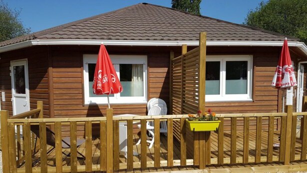 Une cabane en bois avec un toit en tuiles, une terrasse en bois et deux parasols rouges.