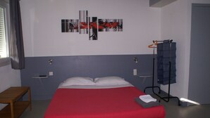 Une chambre à coucher comprenant un lit, une table de chevet, un tableau décoratif, un porte-manteau et une fenêtre avec des rideaux.