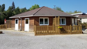 Une cabane en bois avec un toit en tuiles, une terrasse en bois et une allée gravillonnée.