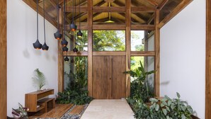 A wooden interior with a large wooden door, hanging pendant lights, and potted plants. - Villa Melody (Cóbano)